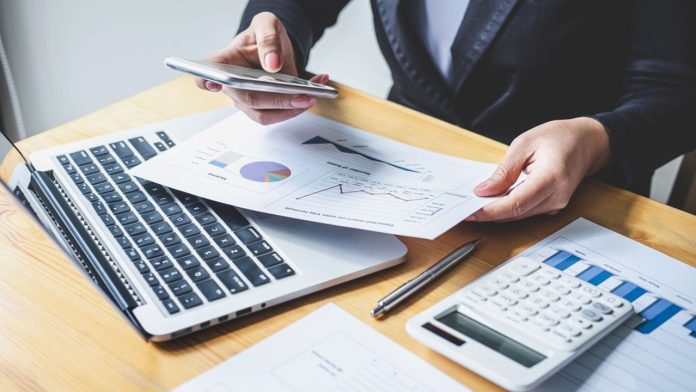 Midsection Of Businesswoman Using Mobile Phone While Analyzing Data On Desk In Office